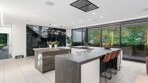A modern kitchen with a large island, bar stools, and a view of greenery outside.
