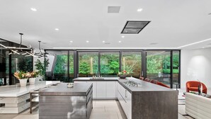 A modern kitchen with a large island, white cabinetry, and large windows offering a view of greenery.