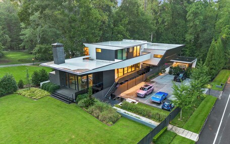 A modern two-story house with a flat roof, large windows, and a covered driveway.