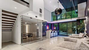 A modern interior with a staircase, a glass partition, a seating area, and a bar with neon lights.