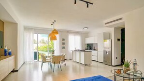 A modern kitchen with white cabinets, a stainless steel refrigerator, and a dining area with a glass table and chairs. - 2Bdrm Apt. Front Juan Dolio Beach Access - Pool+BBQ (Juan Dolio)