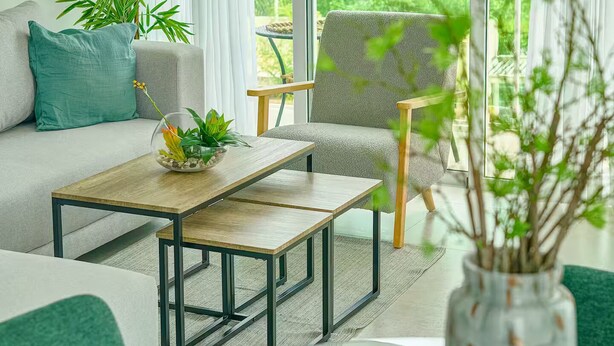 Ein modernes Wohnzimmer mit einer Couch, einem Couchtisch und Blick auf üppiges Grün durch große Fenster.