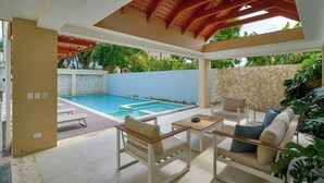 Ein überdachter Außenbereich mit Pool, Sitzgelegenheiten und einer Steinmauer.