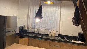Cucina con soffitto in legno, lampadario a sospensione e vista sul verde attraverso una finestra triangolare.