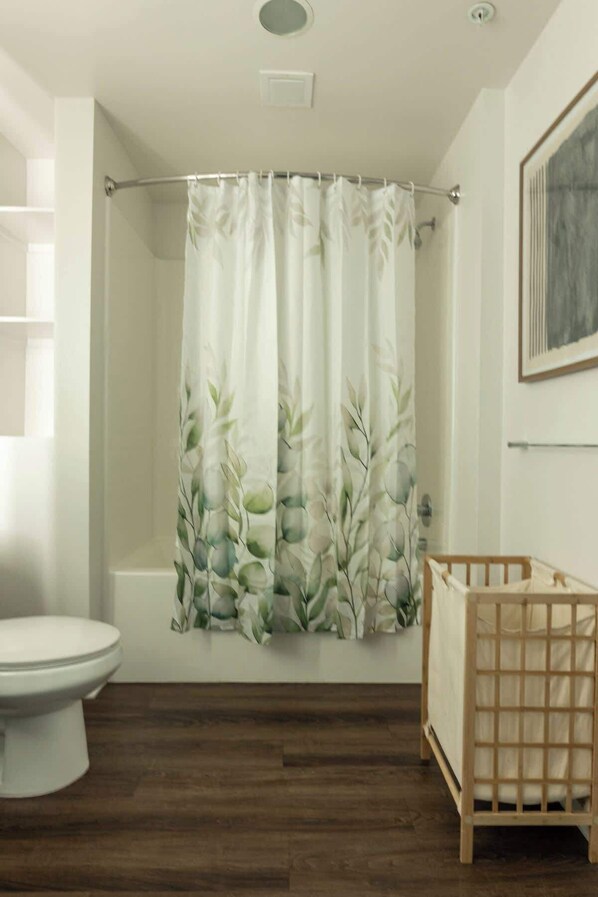 A bathroom with a shower curtain featuring a leaf pattern, a toilet, and a wooden crib. - Modern Apartment w/ Pool & Gym, Near The Americana (Glendale)