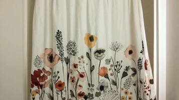 A bathroom with a shower curtain featuring a floral pattern, a toilet, and a small rug on the floor.