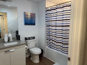 A bathroom with a toilet, a sink, a shower curtain, and a painting on the wall.