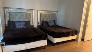 Twee bedden met geborduurde hoofdeinden, een houten vloer en een witte deur.