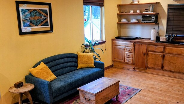 A compact living space with a sofa, a small side table, a wooden chest, and a kitchen area with a microwave and cabinets. - The Gold heart of Grass Valley (Grass Valley)