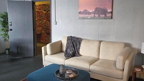 Una sala moderna con un sofá color beige, un reposapiés azul y una alfombra estampada.
