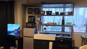 Cocina compacta con refrigerador, estufa y microondas. Un televisor está sobre un mueble a la izquierda y hay una ventana sobre el lavadero.