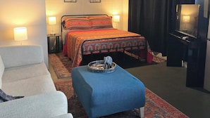 Un dormitorio con cama, sofá, una mesita con un adorno y televisor.