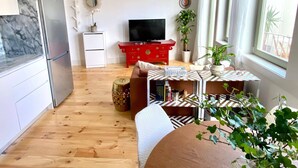 A modern living room with a wooden floor, a red entertainment unit, a flat-screen TV, a white refrigerator, and a dining area with a patterned table. - VIVA - Rooftop Terrace View Flat (Porto)
