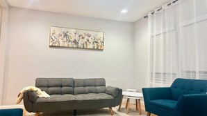 A living room with a grey sofa, a blue armchair, a small white table, and a large floral painting on the wall. - Terrific 2-bedroom house with AC in Dallas (Dallas)