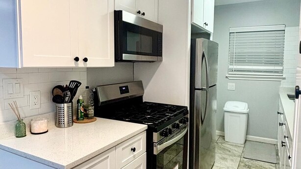 A kitchen with white cabinets, a black microwave, a stainless steel refrigerator, and a tiled floor. - Terrific 2-bedroom house with AC in Dallas (Dallas)