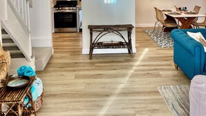 A spacious living area with a staircase, a dining table with chairs, a blue sofa, and a kitchen in the background. - Perfect 2-bedroom beach condo in Oxnard (Oxnard)
