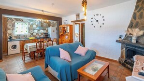 A cozy living room with a blue sofa, a dining area with a table and chairs, a kitchen with patterned tiles, and a fireplace.