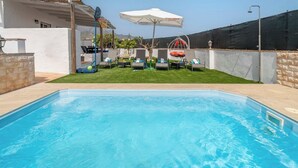 A swimming pool with lounge chairs and a basketball hoop in a backyard setting.