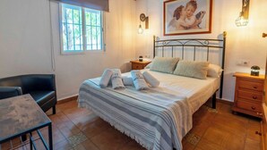A bedroom with a bed, a nightstand, a chair, a table, and a window.