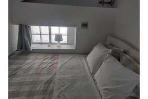 Een slaapkamer met een bed, een raam met uitzicht en een nachtkastje met een lamp.