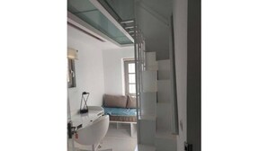 A modern bedroom with a glass shower, a white desk, and a bed with a blue headboard.