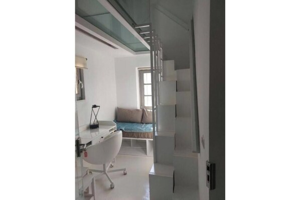 Een moderne slaapkamer met een glazen douche, een wit bureau en een bed met een blauwe hoofdeinde.