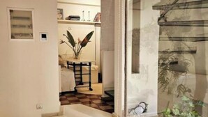 A staircase leading to a room with a checkered floor, a small table with a vase of flowers, and a wall-mounted shelf with decorative items.