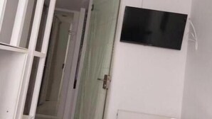 A narrow hallway with a glass door, a white toilet, and a TV mounted on the wall.