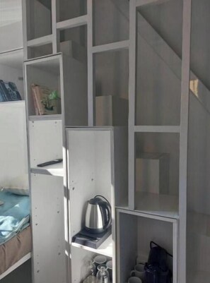 Een kamer met een kitchenette, inclusief een waterkoker, een koffiezetapparaat en een klein kastje met keukengerei.
