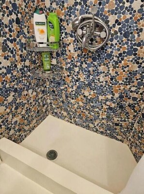 Een badkamer met een wand van kiezelmozaïek, een witte badkuip en een plank met toiletartikelen.