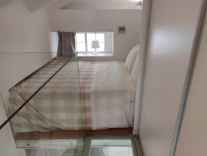Een kleine, smalle kamer met een bed, een raam en een spiegel.