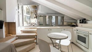 A modern kitchen with a built-in oven, a dining area with a round table and chairs, and a staircase leading to an upper level. - Evangelia3 Attic with Amazing View Patio (Athens)