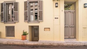 A building with a beige facade, a number '5' on the wall, a door with a lattice pattern, and a potted plant on the sidewalk. - Evangelia3 Attic with Amazing View Patio (Athens)