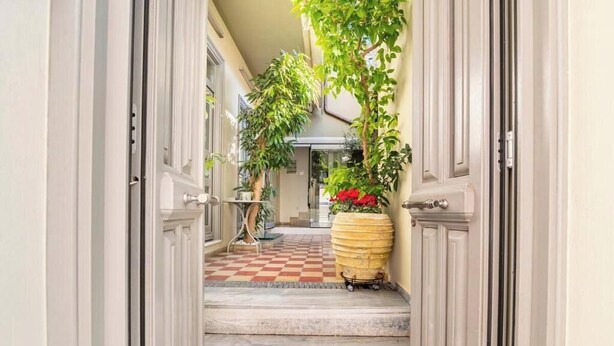 A hallway with a checkered floor, a large potted plant with red flowers, and a door at the end. - Evangelia3 Attic with Amazing View Patio (Athens)