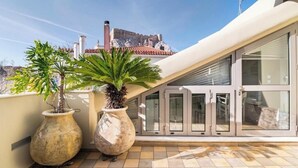 A rooftop terrace with two large potted plants, a glass door entrance, and a view of a historic building in the background. - Evangelia3 Attic with Amazing View Patio (Athens)