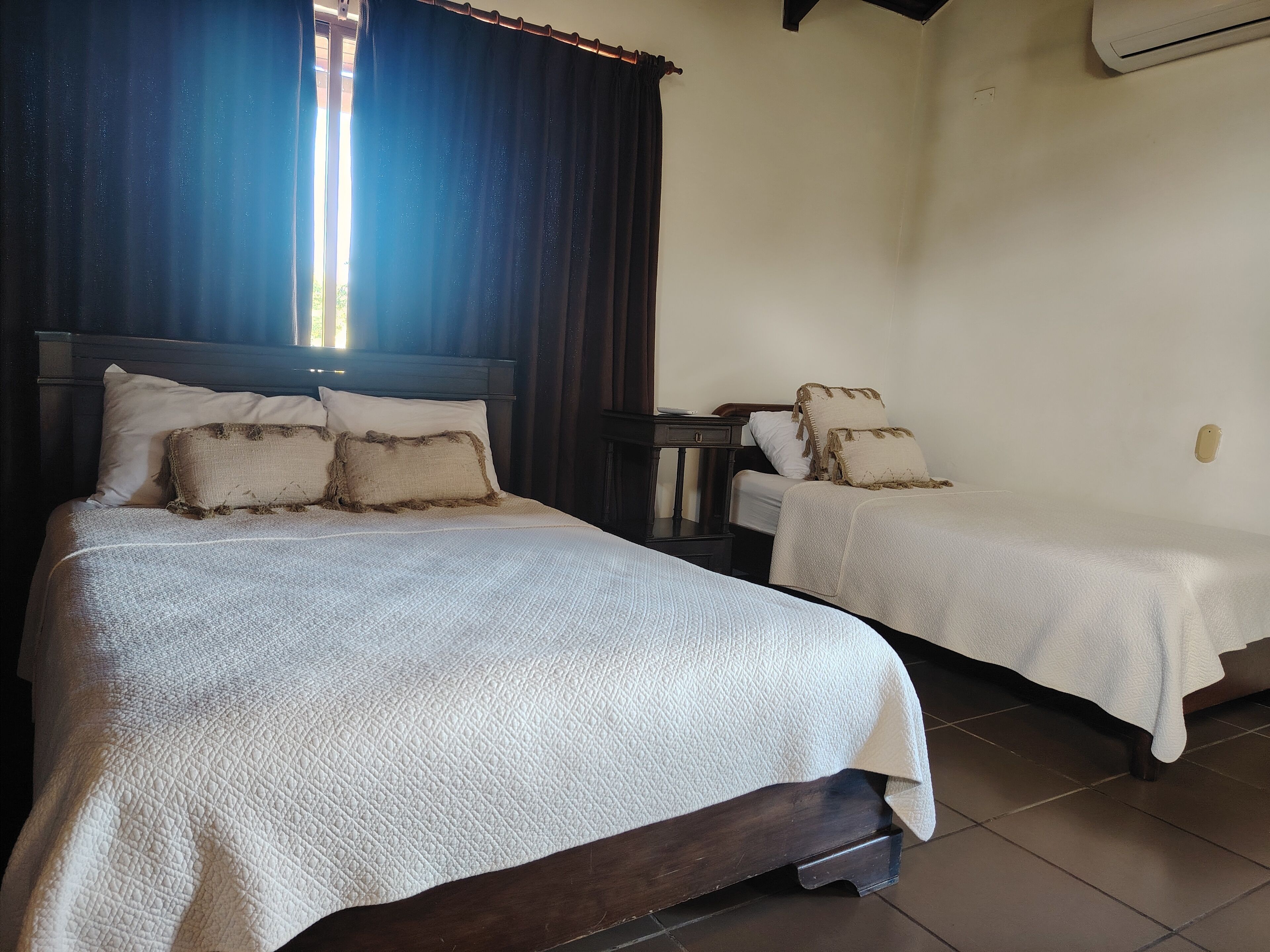Ein Hotelzimmer mit zwei Betten, jeweils mit weißer, strukturierter Bettdecke und passenden Kissen. Dazwischen befindet sich ein kleiner Nachttisch.