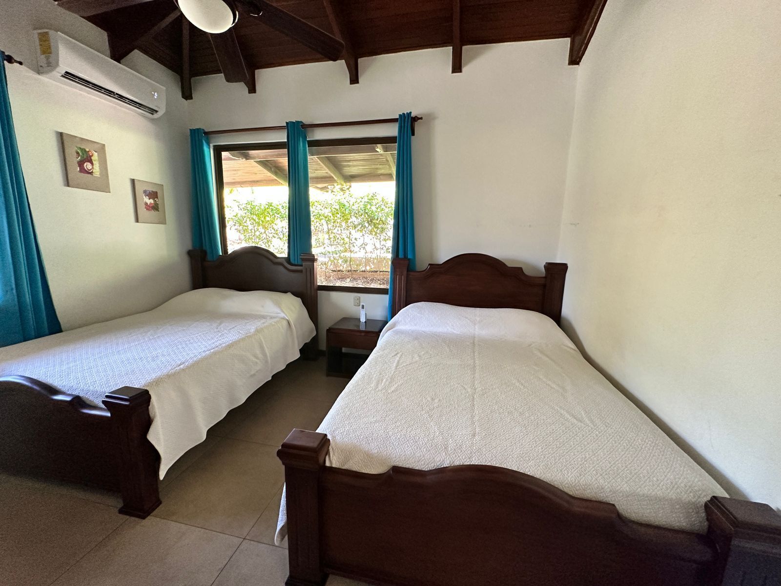 Una habitación con dos camas de madera, una ventana con cortinas y un equipo de aire acondicionado en la pared.