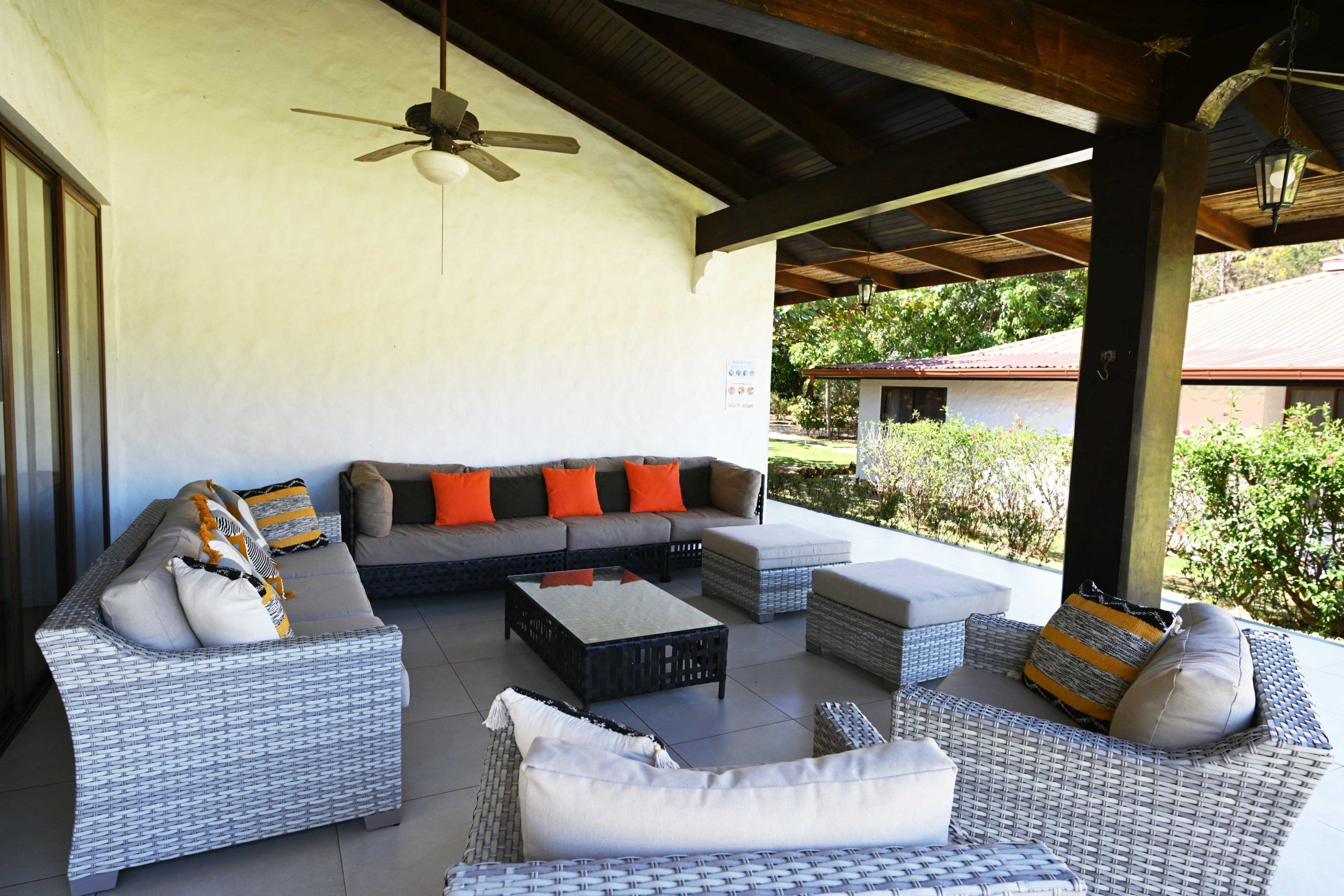 An outdoor patio with wicker furniture, a ceiling fan, and a view of a building in the background.