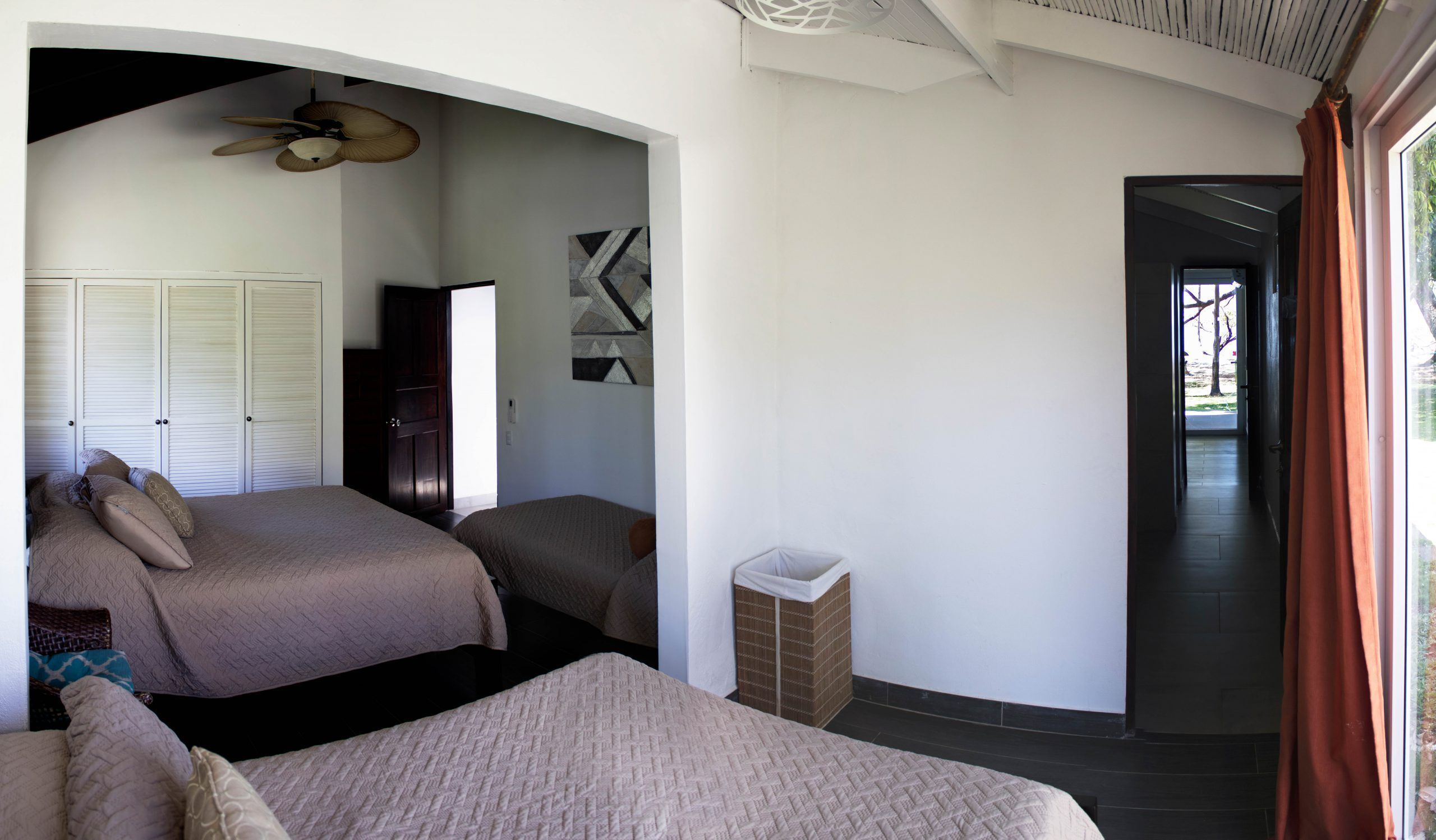 A bedroom with two beds, a ceiling fan, a wardrobe, and a view of the outside.