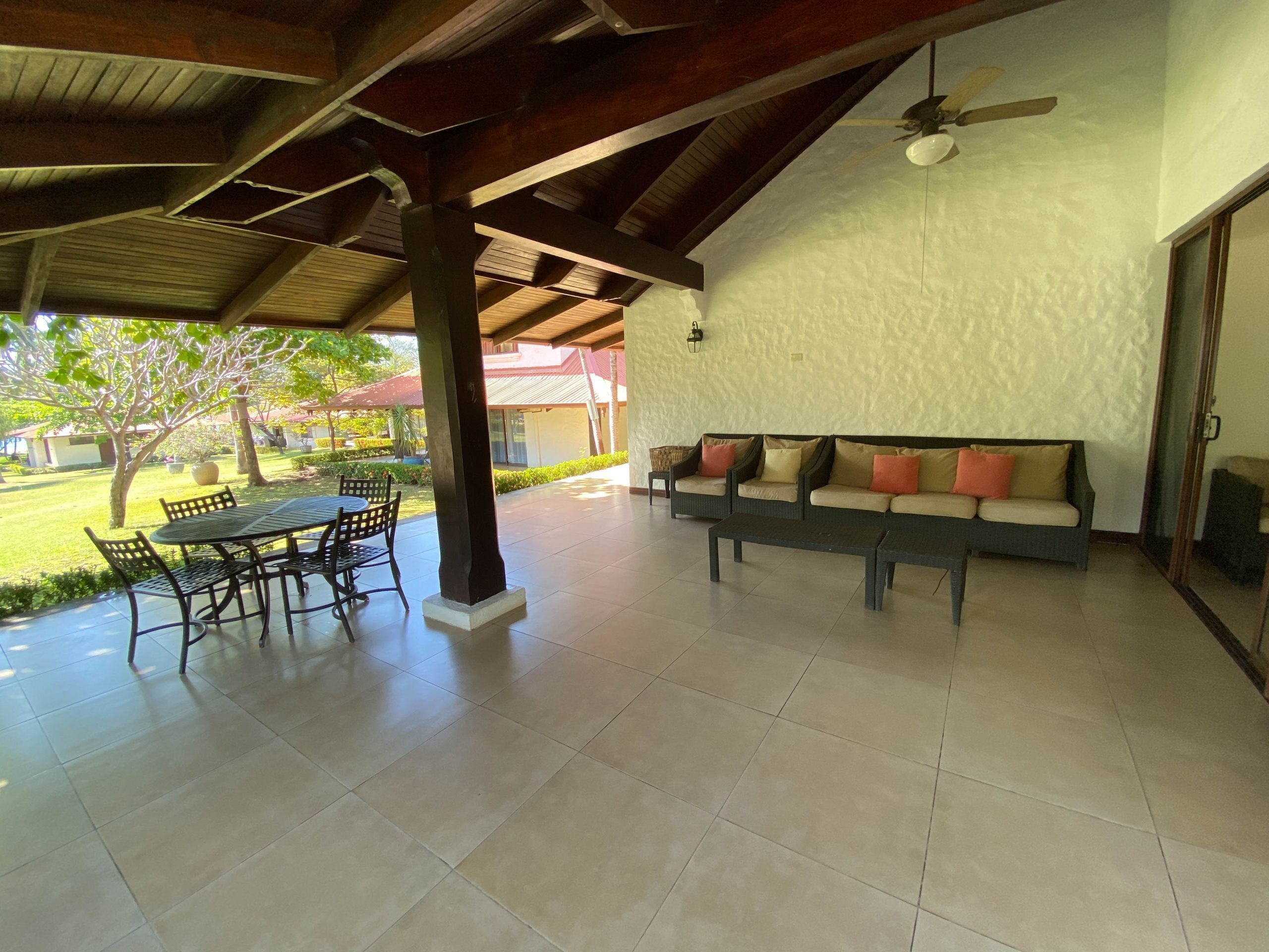 An open patio with a table and chairs, a sofa with cushions, and a ceiling fan.