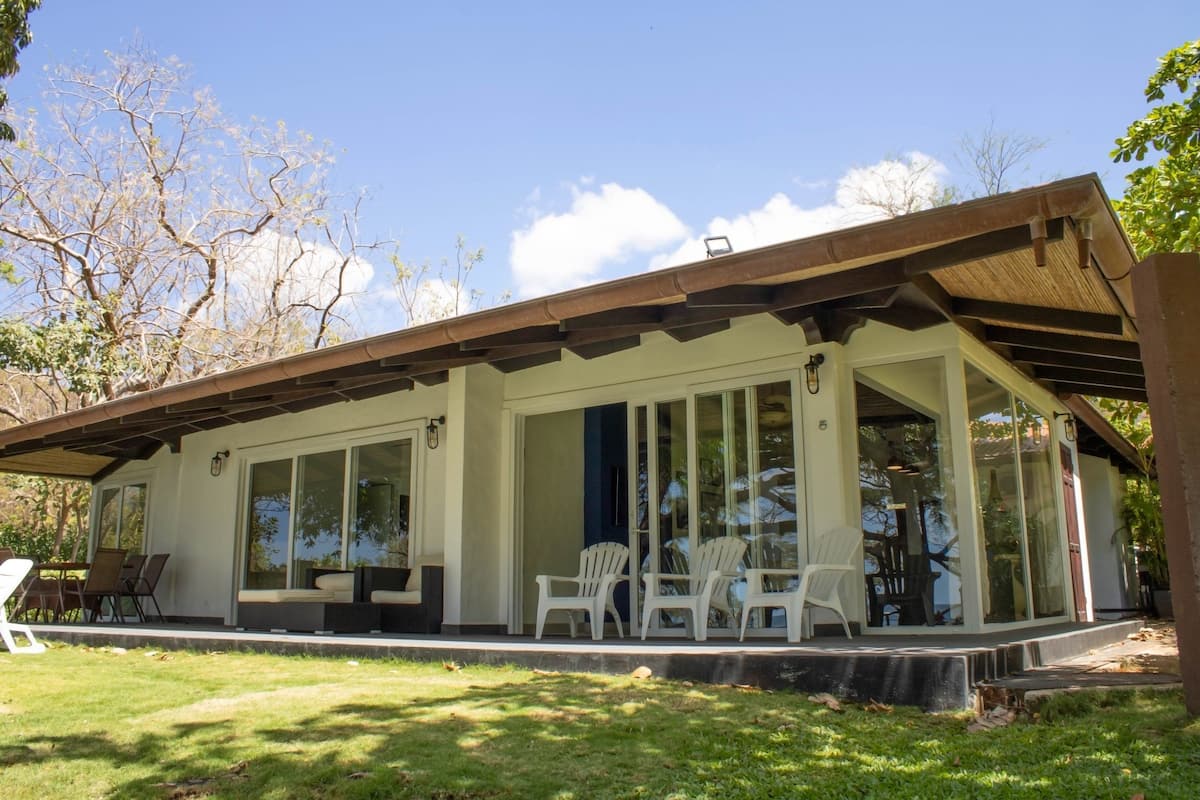 Una casa moderna con porche cubierto, ventanas amplias y mobiliario exterior.