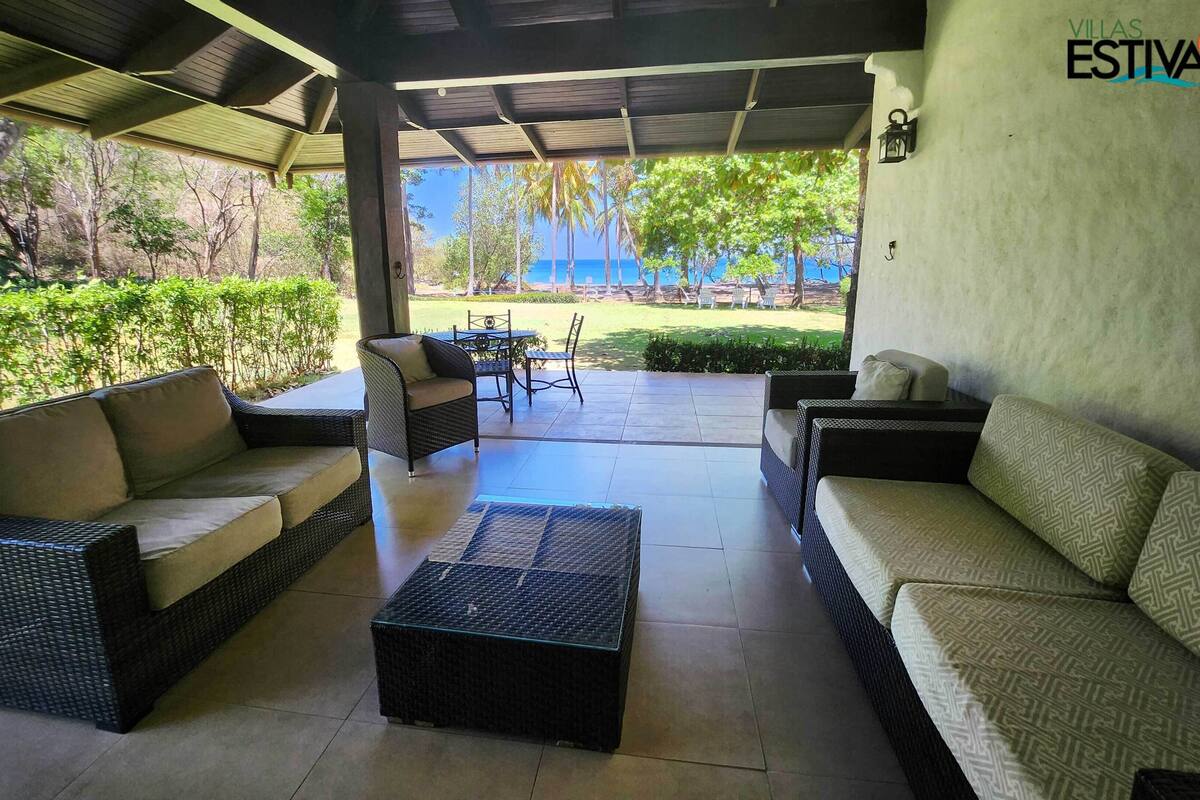 Un espacio de estar al aire libre techado con mobiliario de mimbre y vistas al mar.