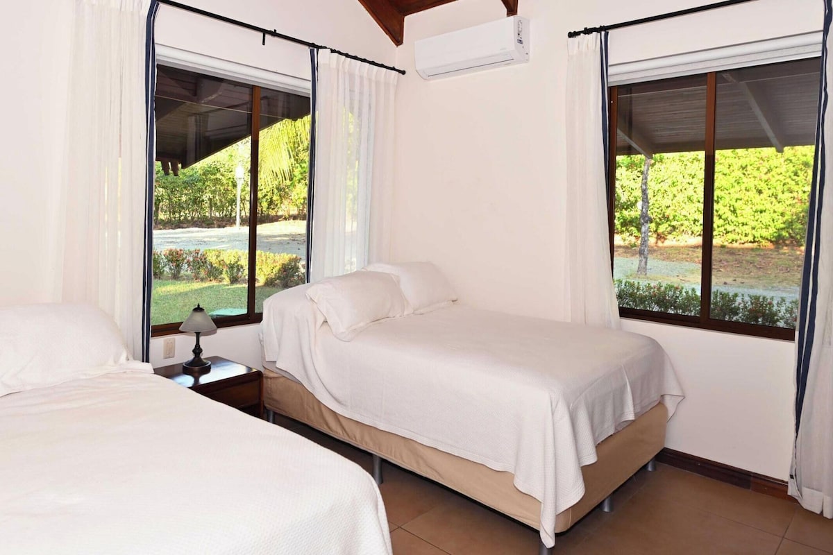 A hotel room with two beds, large windows, and an air conditioning unit.