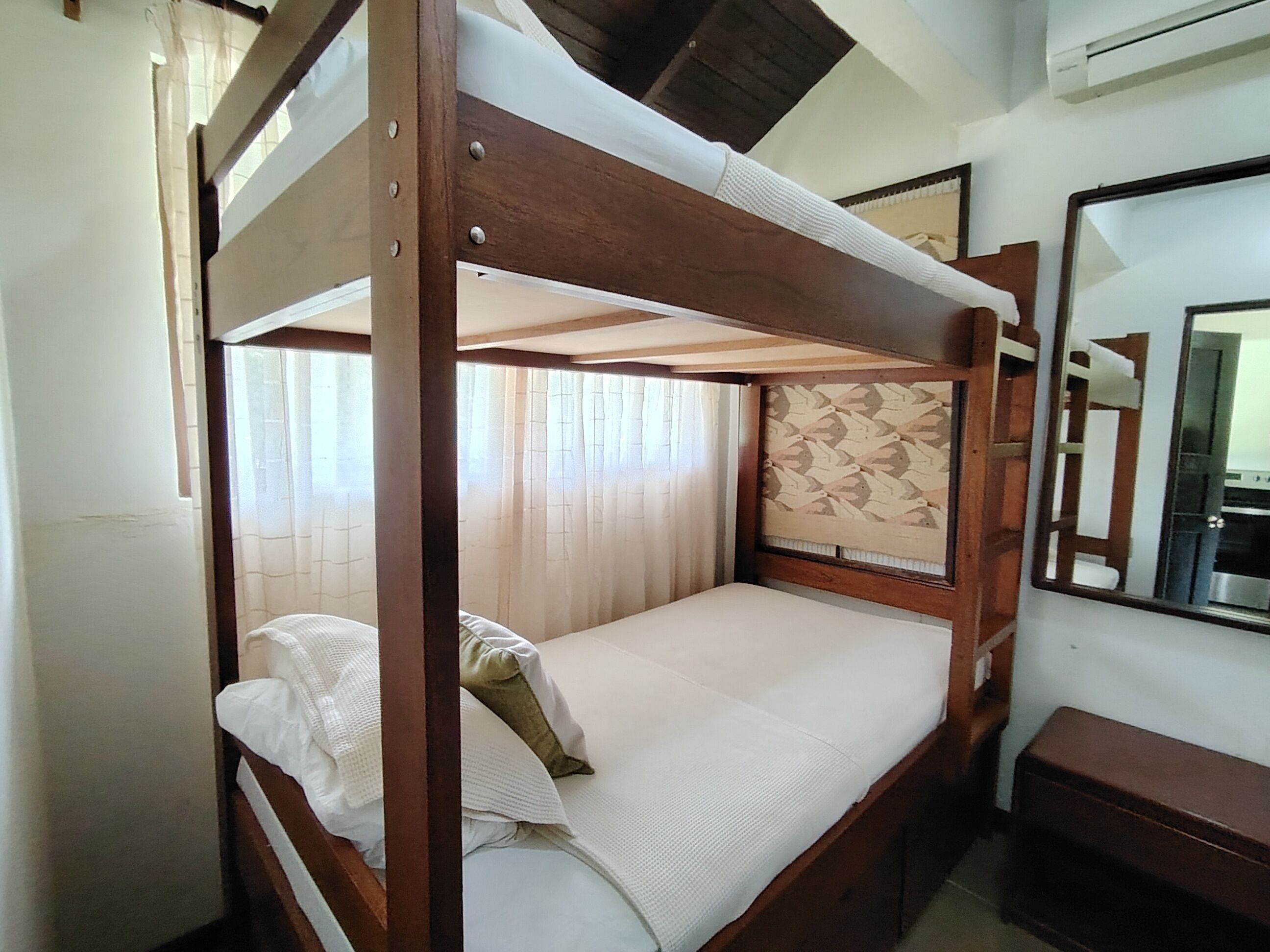 Habitación individual con una cama nido, cabecero de madera, mesita de noche y un espejo en la pared.