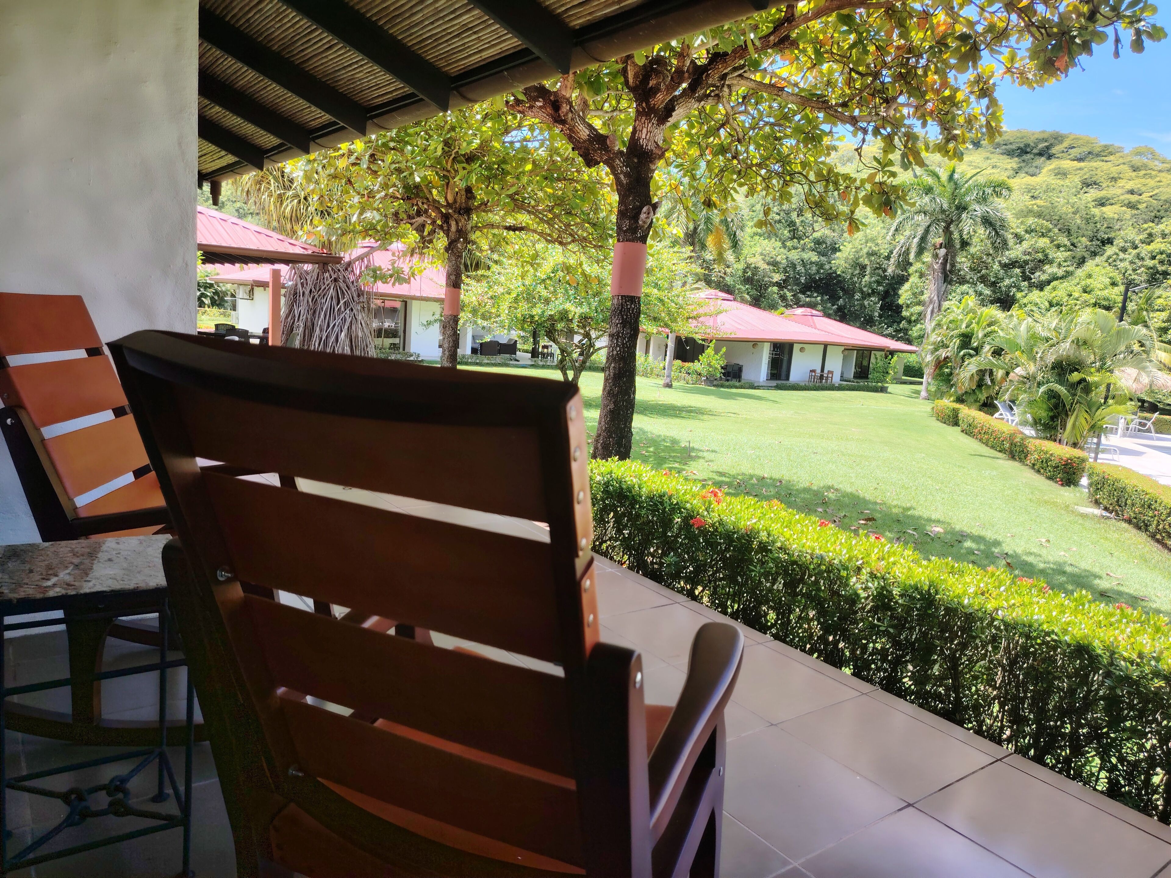 A patio area with a wooden chair, a table, and a view of a well-maintained lawn and buildings in the background.
