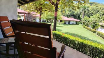 A patio area with a wooden chair, a table, and a view of a well-maintained lawn and buildings in the background.