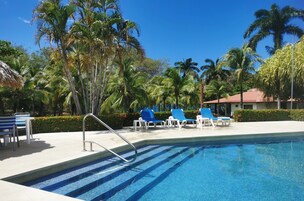 Piscina con azulejos azules, rodeada de palmeras y sillas de descanso azules.