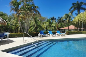 A swimming pool with blue tiles, surrounded by palm trees and blue lounge chairs. - Villas Estival Playa Prieta (Tempate)