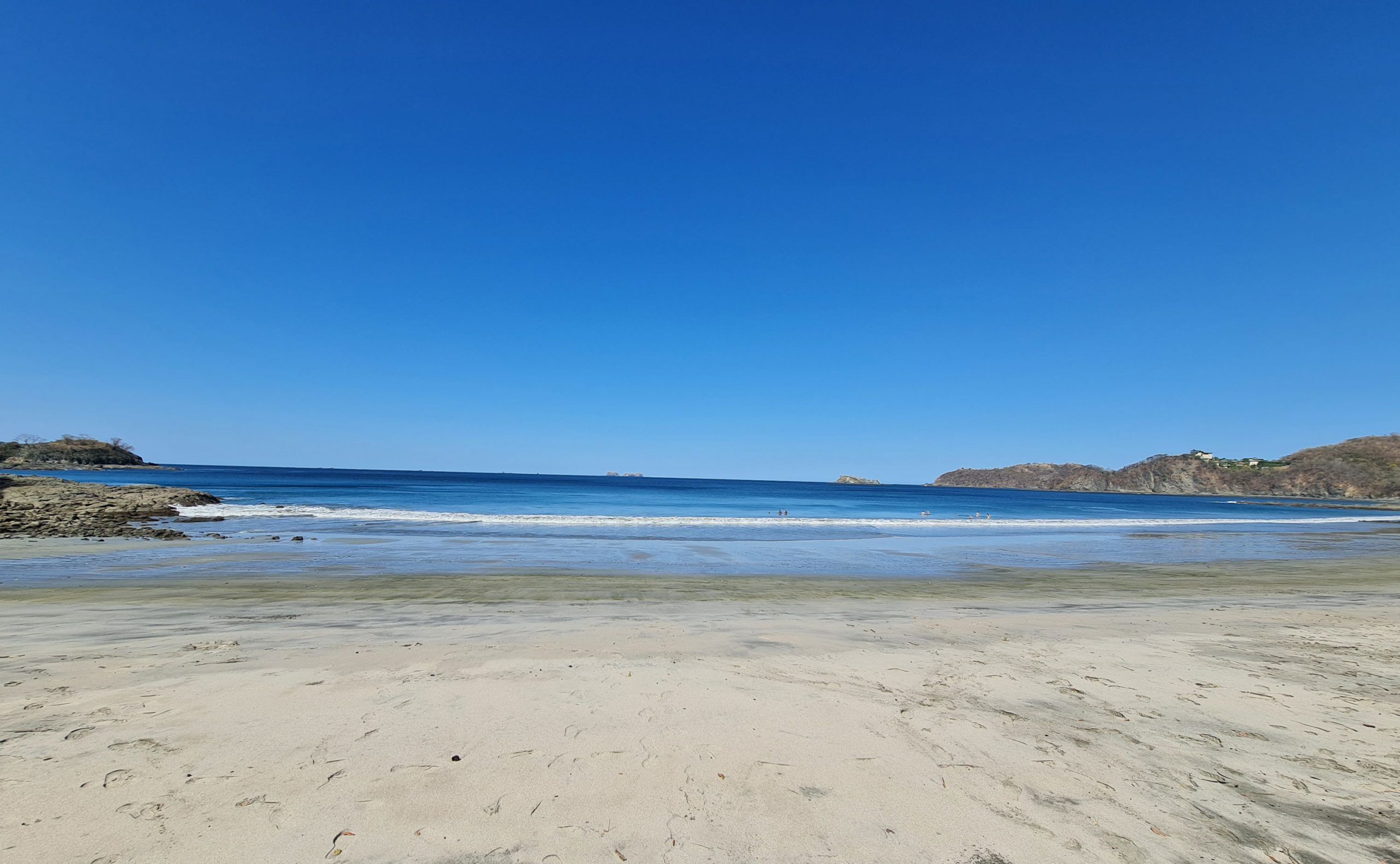 Una playa con cielos despejados, aguas tranquilas y afloramientos rocosos.