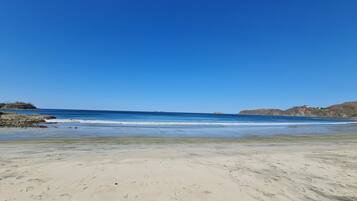 Una playa con cielos despejados, aguas tranquilas y afloramientos rocosos.